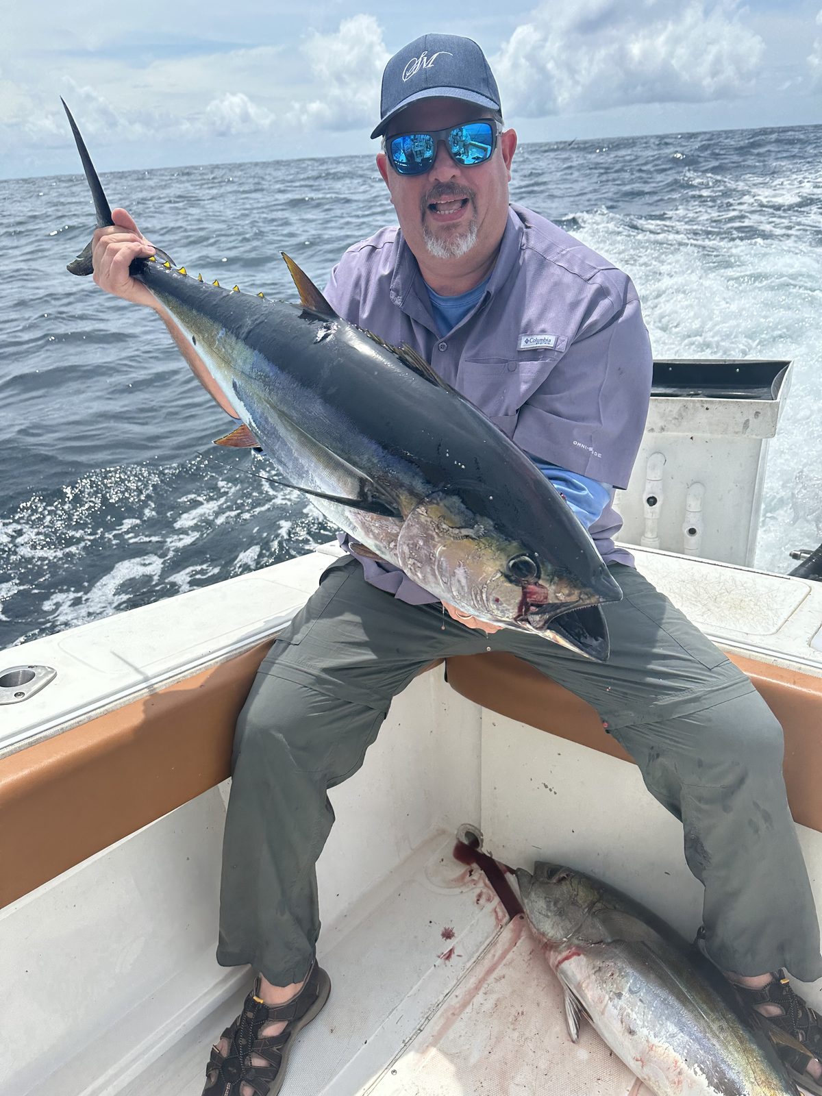 A man holding a yellowfin tuna in the stern of a fishing boat